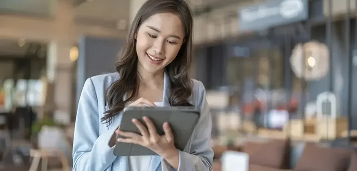 Businesswoman smiling while using a tablet in a spacious modern cafe.