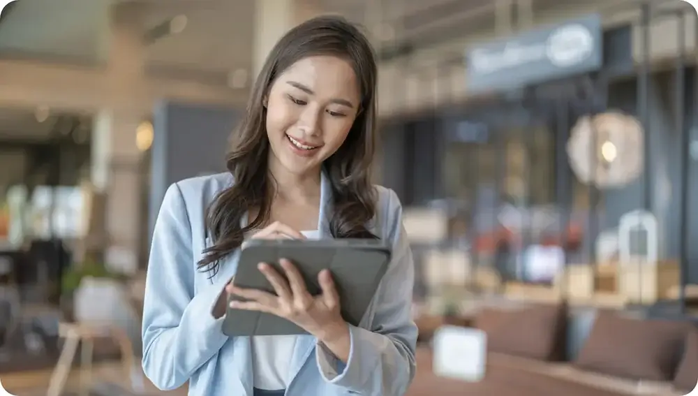 Businesswoman smiling while using a tablet in a spacious modern cafe.